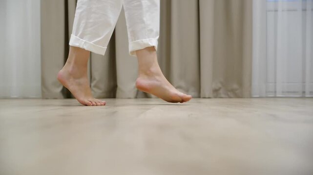 Young woman walking tiptoe barefoot on a warm wooden floor at home