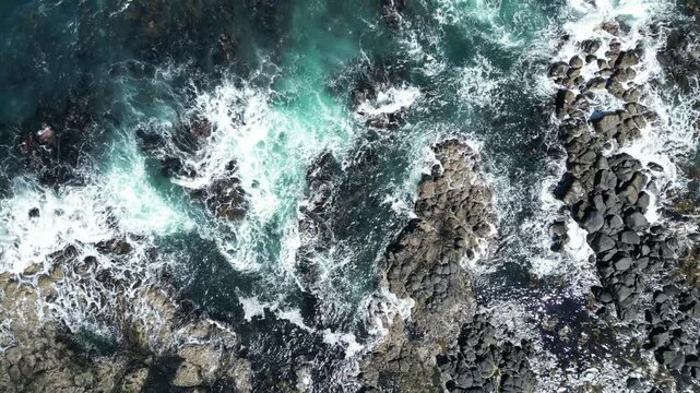 Aerial drone view of powerful ocean waves crashing against the rugged rocky coastline of Northern England, dramatic seascape with turquoise water, white sea foam, and natural coastal landscape