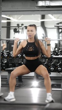 Fit woman performing wide stance squat on Smith machine during lower body strength workout in modern gym. Functional fitness, bodybuilding and leg training.