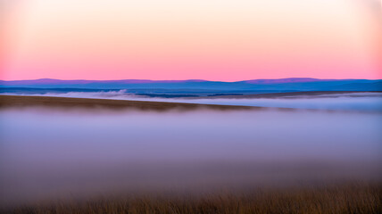 Fototapeta premium Foggy landscape with rolling hills at sunrise or sunset