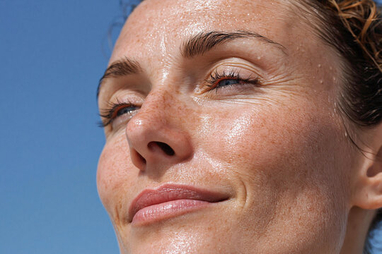 Glowing dewy freckled female cheek close up with sunlit skin texture and subtle smile, natural radiance and fine lines visible