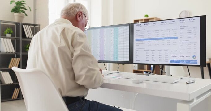 Senior man accountant analyst working on computer. Office view with monitors and spreadsheet finance data for analysis, auditing records and numbers. Concept of financial data analysis.