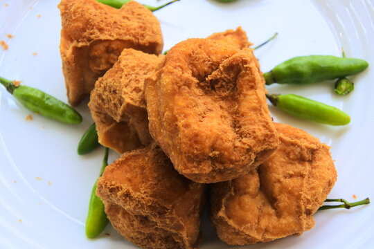 Deep fried tofu or tahu sumedang served with green bird's eye chili on a white plate.