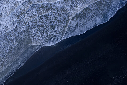 Aerial view of the black sand beach with white sea foam and crashing waves along the coastline, Hornafjordur, Iceland.