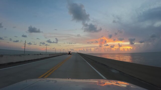 Driving a car on Overseas Highway bridge stretching over the water during a vibrant sunset in Florida, United States
