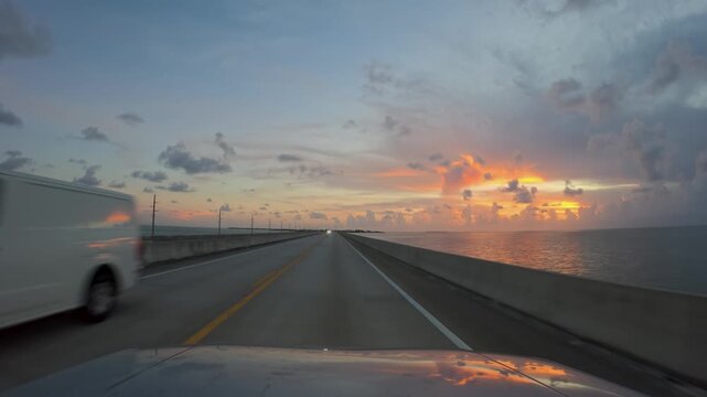 Driving a car on empty Overseas Highway bridge stretching over the water during a vibrant sunset in Florida, United States