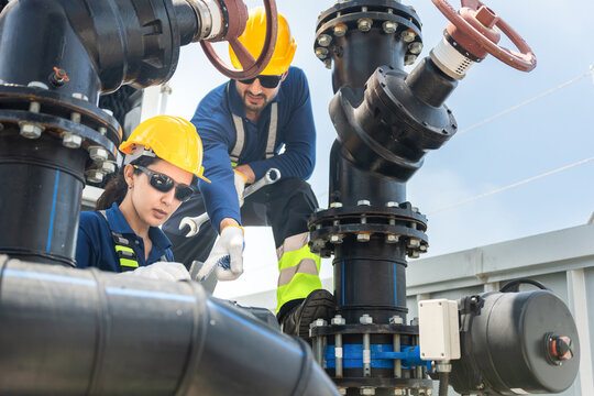 Industrial engineers team in safety gear inspecting large water pipe system at treatment plant, Team of professional technicians monitoring industrial plumbing with digital tablet and wrench