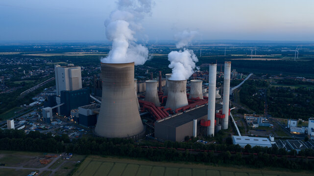 Aerial view of Kraftwerk Niederaussem with its large cooling towers emitting steam plumes over industrial infrastructure in Bergheim, Nordrhein-Westfalen, Germany.