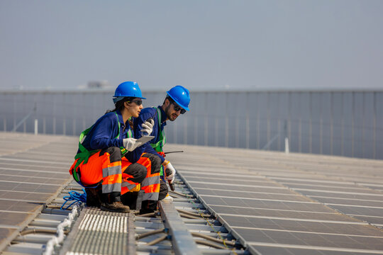 Solar technicians inspecting solar panels on a rooftop, Renewable energy team working on solar power plant installation, Engineers using tablet and radio for rooftop solar array maintenance