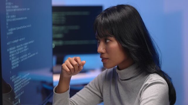 Asian woman developer thinking deeply while debugging code on computer screen, solving software problem and planning solution in tech office with multiple monitors