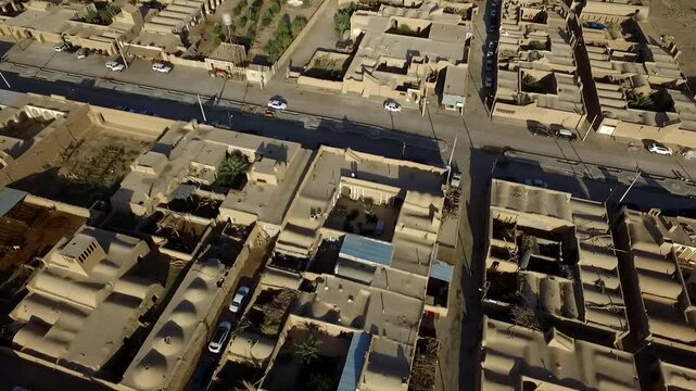Professional drone shot focuses on dense desert village center with streets and rooftops surrounded by barren land.
