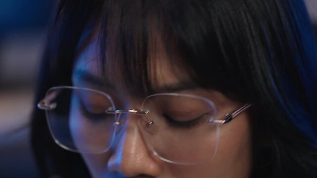 Extreme close up of Asian woman eyes wearing blue light blocking glasses while looking at computer screen, digital eye strain and eye health from long screen time