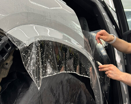 A car wrapping specialist applies a polyurethane film to the car. Detailer smoothes PPF. Car wrapping, detailing, tuning and styling. PPF protective film against chips and scratches. Protects the car.