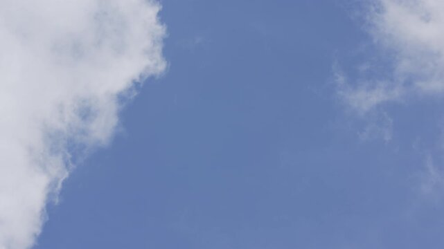 Soft organic clouds passing through clear blue sky in real time during daytime, low angle view with peaceful serene mood, suitable for typography background.