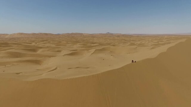 High quality aerial footage of rolling desert sand dunes with soft curves and distant mountain hints on horizon.