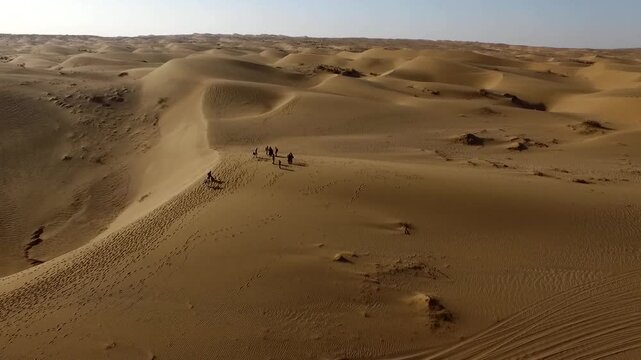 Beautiful aerial panorama of desert sand dunes with tiny figures traversing the ridge emphasizing isolation.