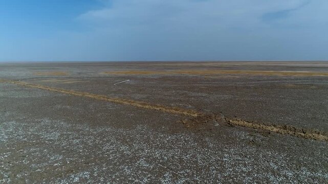 Panoramic aerial video of vast desert salt marsh showing textured ground and distant horizon under clear sky.