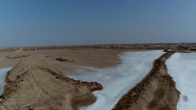 High angle aerial view captures expansive salt marsh with white crystalline surface and brown earth patches under bright daylight in remote desert area.