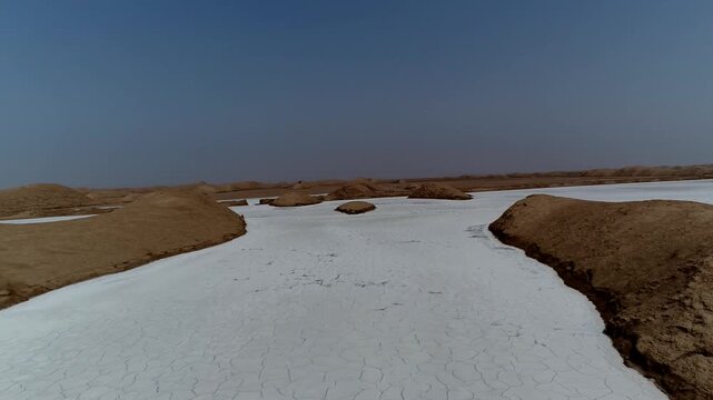 Aerial drone footage shows vast white salt marsh with dark earth formations and shallow water pools in arid desert under clear blue sky creating striking contrast landscape.