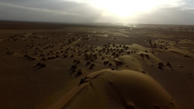 Detailed aerial footage of desert plain with textured sand surface and small scattered dunes under warm sunlight.
