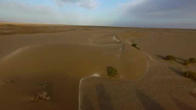 Dynamic aerial perspective of desert plain with wind patterns and isolated dune clusters.