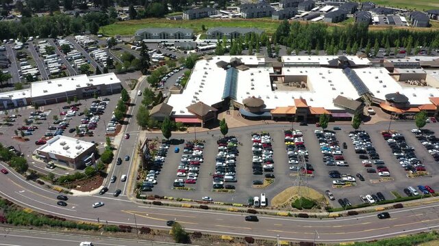 4K aerial drone footage of a busy outlet shopping center in Woodburn, Oregon, USA during the Juneteenth holiday with crowded parking lots, retail stores, and shoppers