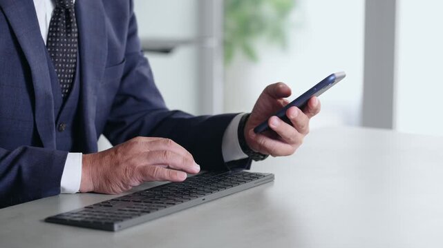 スマホとPCを使って作業する男性。アプリ、ビジネス、SNS、仕事、業務、開発、データ、DX、IT