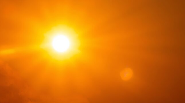 Intense summer sun glowing brightly in a clear orange sky creating a strong lens flare effect with radiant warmth and heat distortion for meteorological concepts