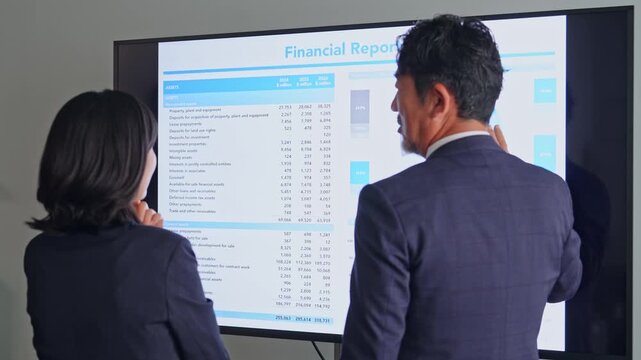 画面を見ながら会話するビジネスパーソンのグループ。会議、チームワーク、同僚、人材、相談、研修、指導
