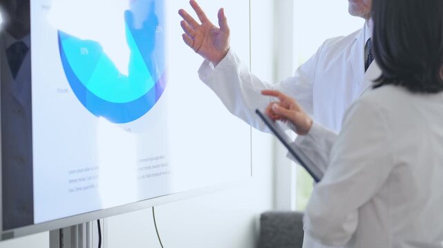 A group of men and women in lab coats holding a meeting while looking at a screen. Science, research, medical, university, investigation, materials, data, analysis, experiment.