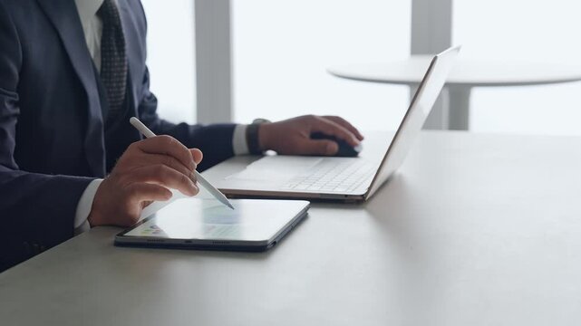 ノートパソコンとタブレットPCを使って作業する男性。DX、IT、オフィス、仕事、作業、デスクワーク