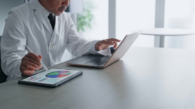 ノートパソコンとタブレットPCを使って作業する白衣の男性。科学、研究、医療、医師、実験、データ、分析