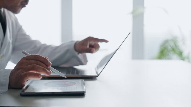 A man in a white coat working with a laptop and a tablet PC. Science, research, medical, doctor, experiment, data, analysis.