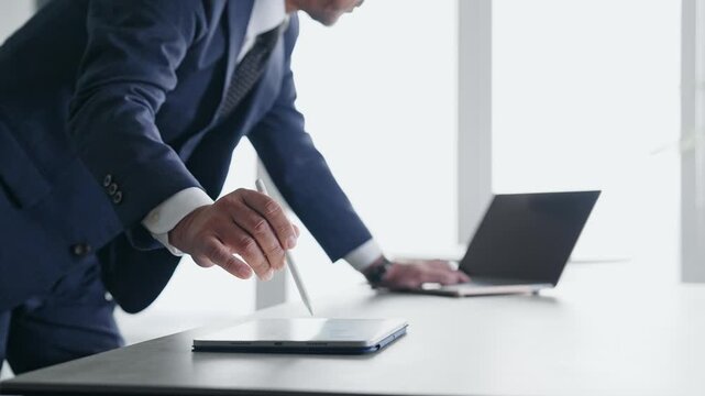 ノートパソコンとタブレットPCを使って作業する男性。DX、IT、ビジネス、オフィス、タッチペン、作業