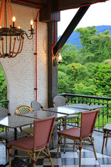 Fototapeta premium Empty bistro tables and woven chairs sit quietly on a balcony, waiting for guests to enjoy a meal overlooking the lush tropical forest and distant mountains.
