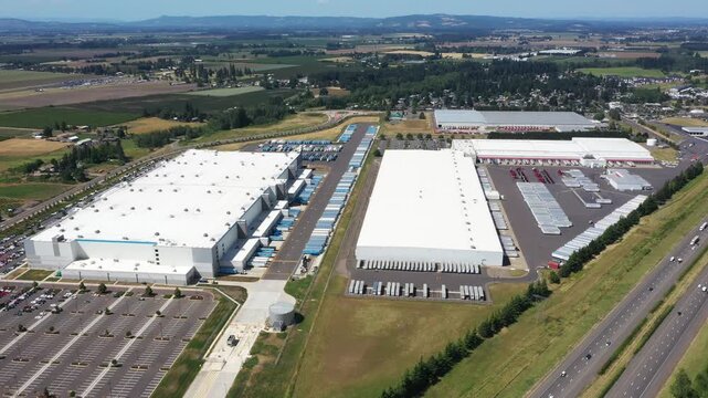 4K aerial drone footage of a major ecommerce fulfillment center and grocery distribution warehouses in Woodburn, Oregon, USA with numerous semi trucks, loading docks, and logistics operations