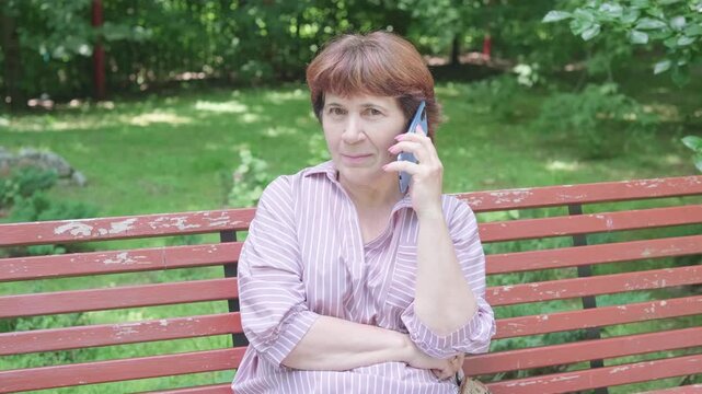 senior woman talking on mobile phone on park bench looking away. pensive senior woman misses adult child who moved far away. lonely senior woman seeks family connection through call
