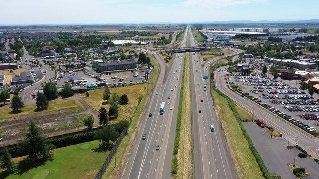 4K aerial drone video footage of Interstate 5 near Woodburn, Oregon, USA on a clear summer day, featuring traffic flow, surrounding commercial district, green spaces,  a popular outlet shopping center