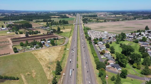 4K static aerial drone footage looking north over Interstate 5 near Woodburn, Oregon, USA, showing busy summer traffic, farmland, neighborhoods, and Willamette Valley landscape