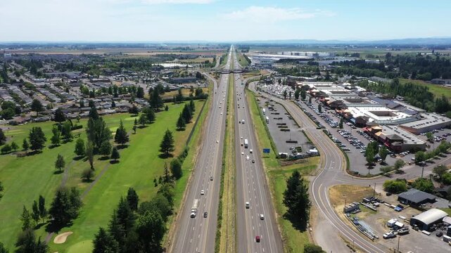 4K aerial drone video footage of Interstate 5 near Woodburn, Oregon, USA on a clear summer day, featuring traffic flow, surrounding commercial district, green spaces,  a popular outlet shopping center
