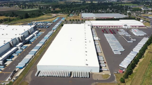 4K aerial drone footage of a major ecommerce fulfillment center and grocery distribution warehouses in Woodburn, Oregon, USA with numerous semi trucks, loading docks, and logistics operations
