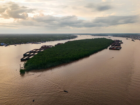 Aerial view of Pulau Kembang surrounded by the Barito River with coal barges and lush vegetation under a golden sunset sky in Alalak, South Kalimantan, Indonesia.