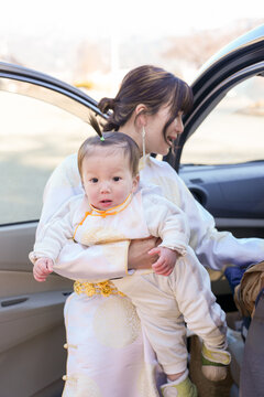 Young mother smiles warmly while holding her baby. Baby dressed in soft, elegant traditional attire. Sunlight glows gently on their faces, capturing a tender moment
