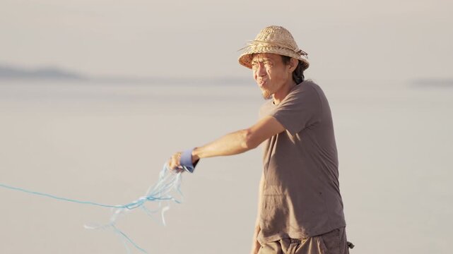 an asian fisherman casting or throwing a fishing net in the ocean in indonesia, southeast asia, medium slow motion shot