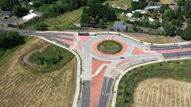 4K static aerial drone footage of a modern roundabout in Woodburn, Oregon, USA with light traffic, landscaped center island, surrounding roads, farmland, and residential neighborhood