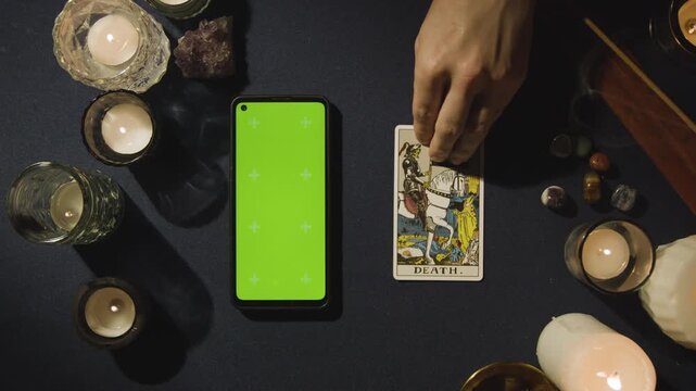 Overhead Shot of Person Giving Tarot Card Reading with Green Screen Smartphone Next to Death Tarot Card on Table