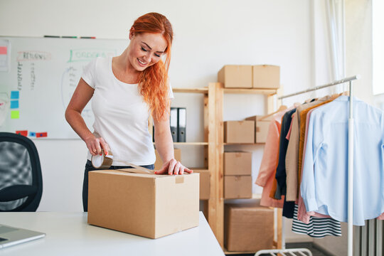 Young woman packing cardboard box for online clothing order