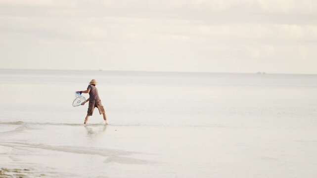 Indonesian fisherman throwing fishing net in sea or ocean to catch fish close to beach, indonesia, southeast asia, asian people, slow motion shot