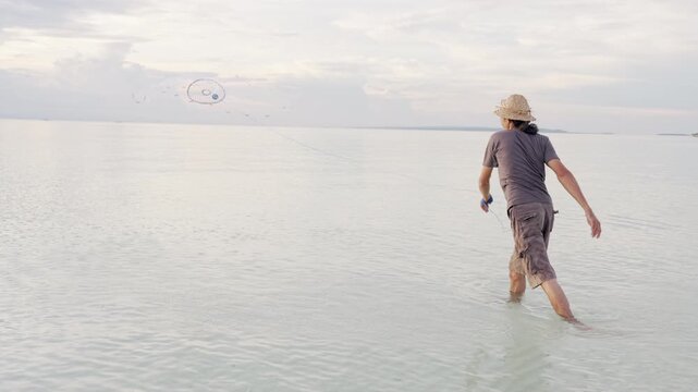 a fisherman in indonesia throwing or casting a fishing net in ocean, indonesian people, southeast asia, slow motion shot