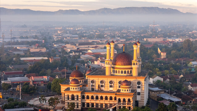 Kecamatan Klaten Utara, Jawa Tengah, Indonesia - 02 July 2026: Aerial view of Al Aqsha Great Mosque Klaten with its domes and minarets rising above the urban landscape and misty hills.